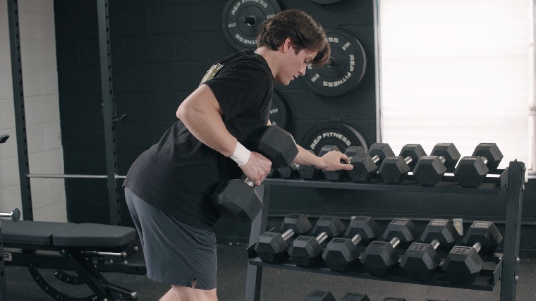 A BarBend tester bracing against the REP Fitness Dumbbell Storage Rack for dumbbell rows.